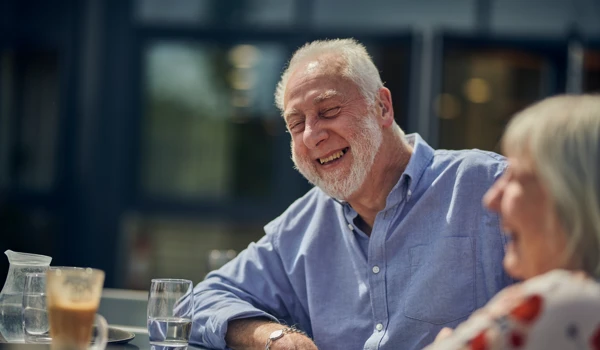 Smiling Older Man And Woman Sitting Together Outdoors At Table In The Sunshine