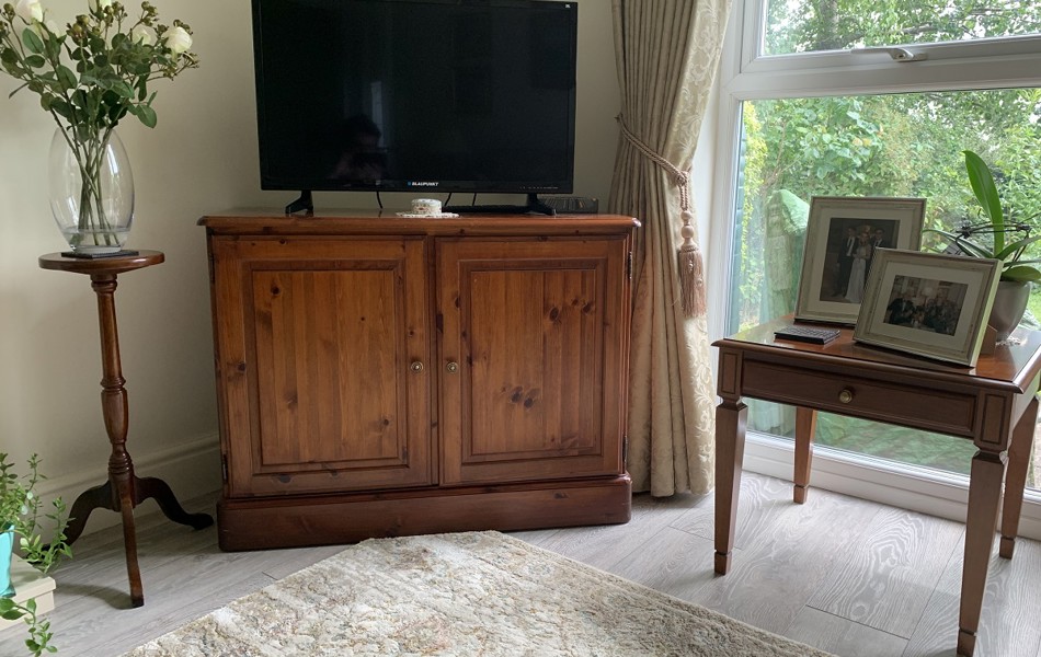 A bright living room with flowers on a stand beside flat screen tv