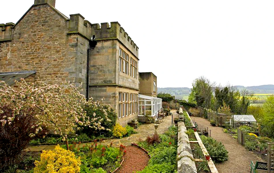 A grand stone building with turrets and beautiful gardens