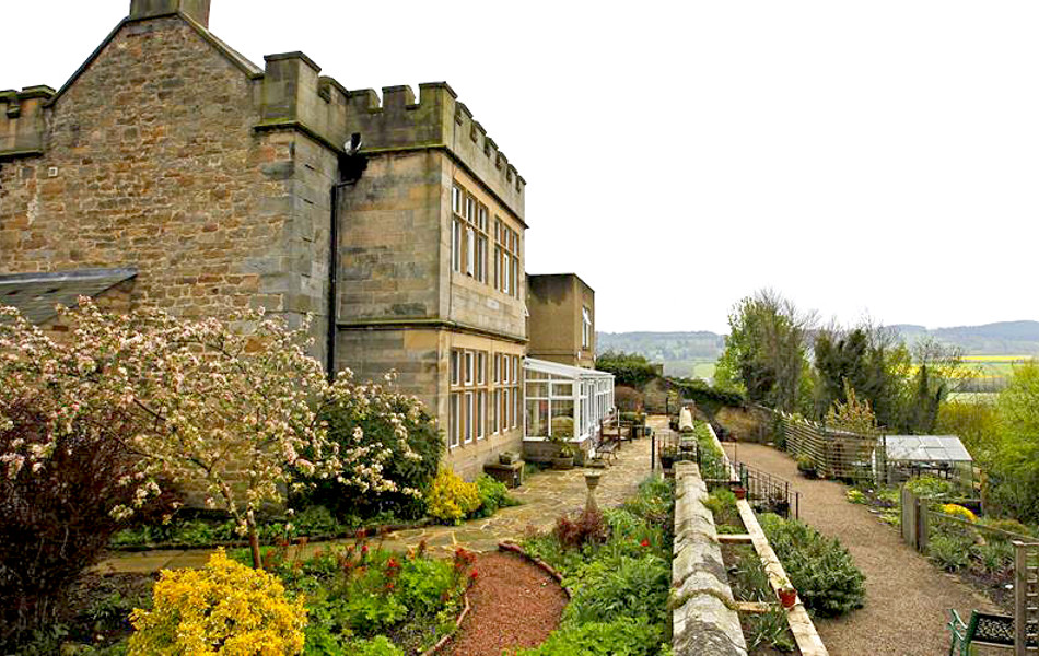 A grand stone building with turrets and beautiful gardens