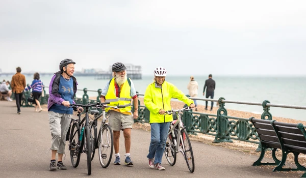 Group Of Older People Pushing Bikes On Sea Front