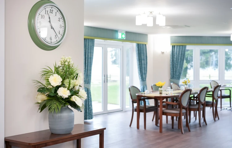 Bright and welcoming dining room at Westall House Residential Care Home in Horsted Keynes, with set tables, comfortable chairs, and a large clock on the wall.