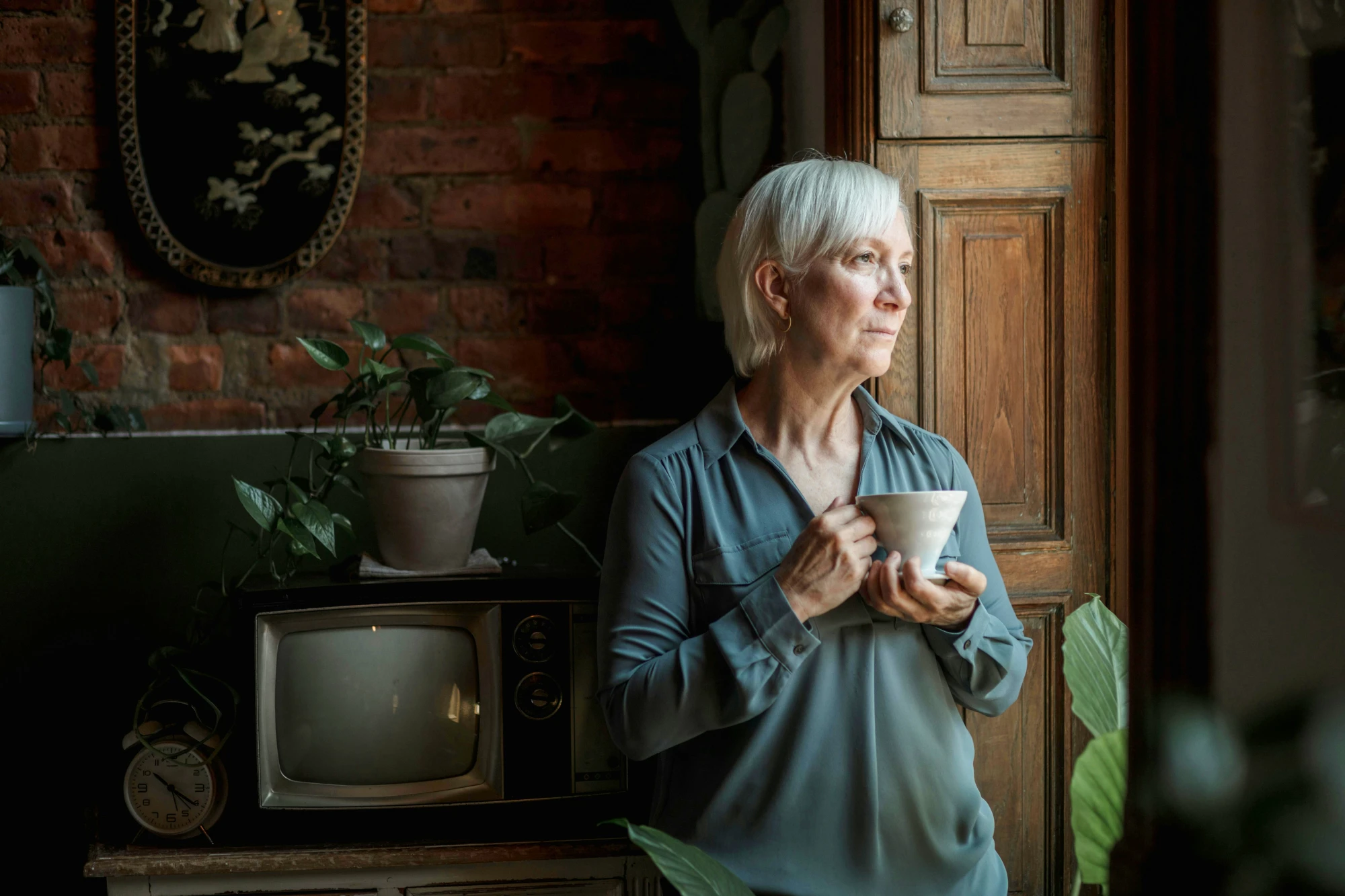 Older woman looking out of window holding a hot drink