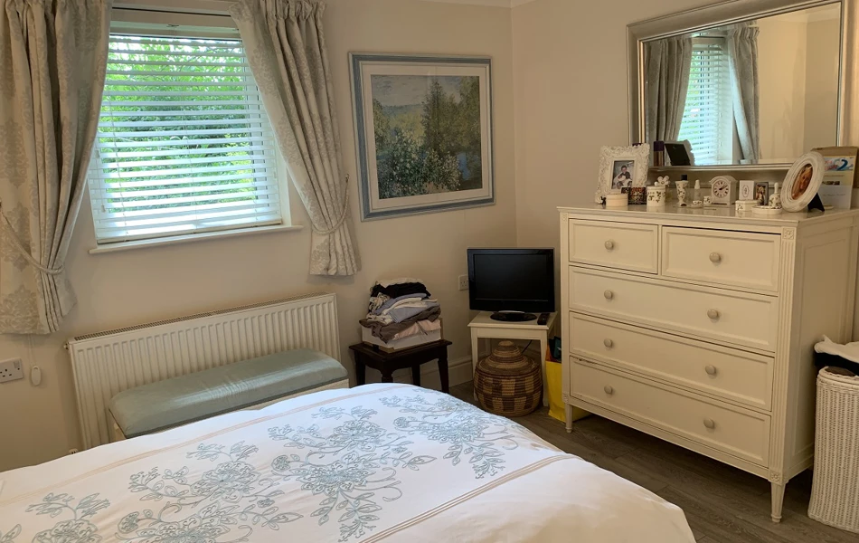 A large resident bedroom at The Firs Complex with a chest of draws, small tv and bed