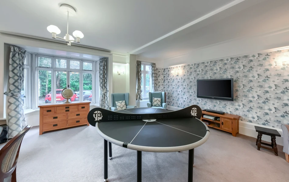 Table tennis table, comfortable armchairs, and a large television in the activity room at Westall House Residential Care Home in Horsted Keynes.