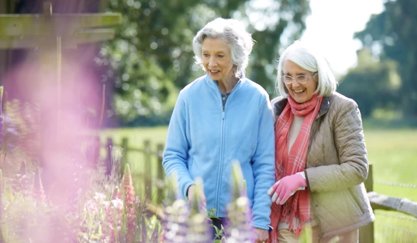 Two Older Ladies Walking In The Sunshine In A Beautiful Garden