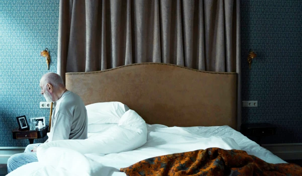 Older Man Sitting On Edge Of Bed