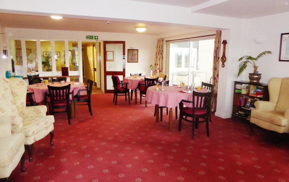 Bright dining area with red carpet and round tables at Abbeyfield House sheltered housing in North Yorkshire