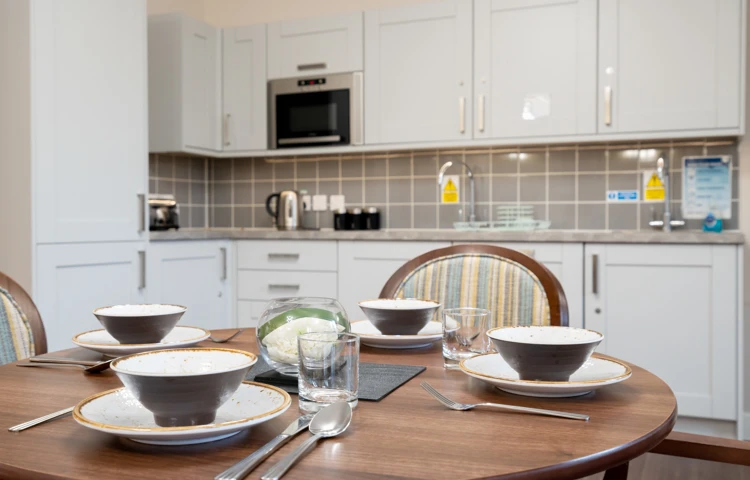 Dining table set for a meal in a modern dining room at Westall House, with kitchen cabinets in the background